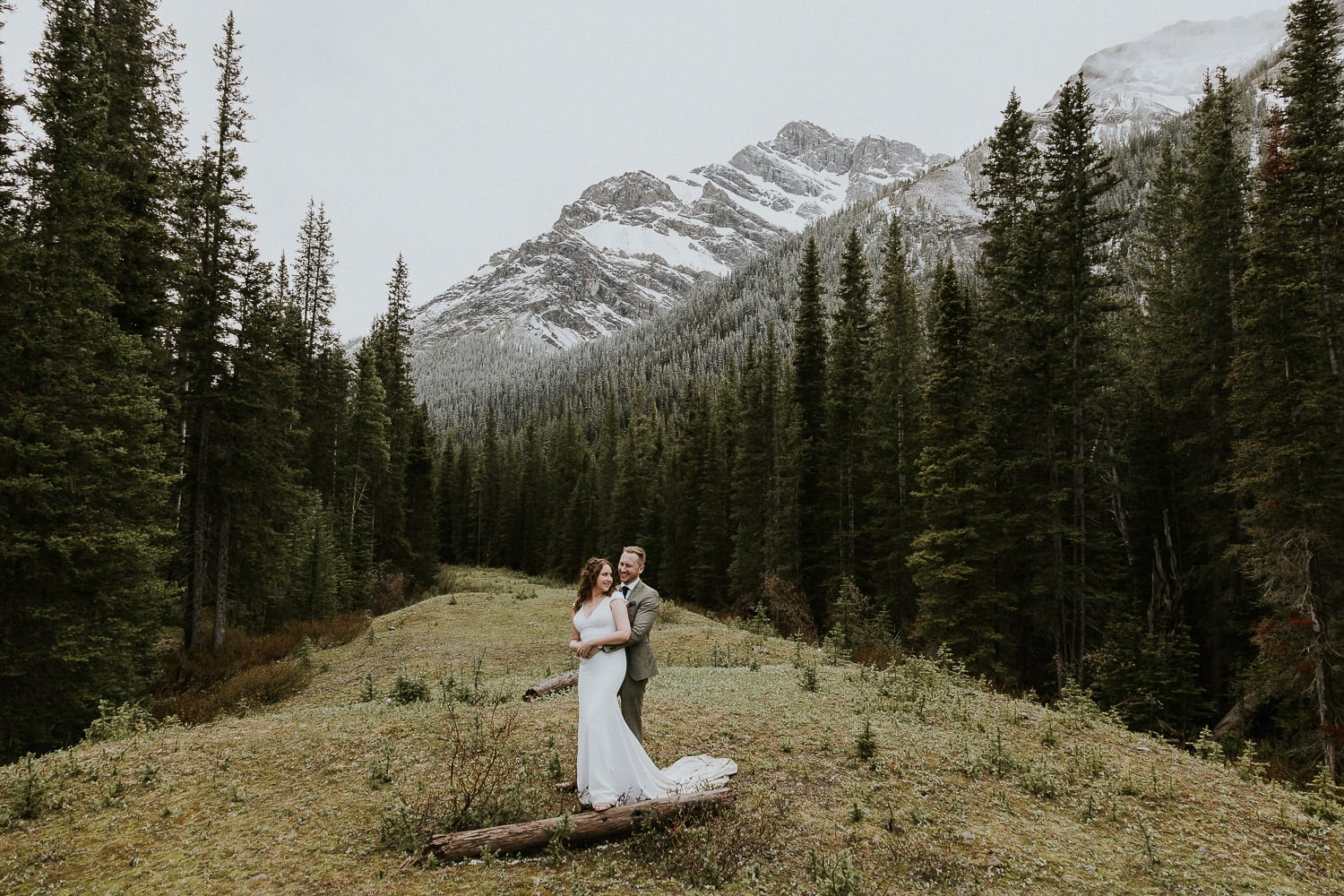 Bride and Groom hugging in the middle of a forest with a mountain behind them in Kananaskis Alberta 1