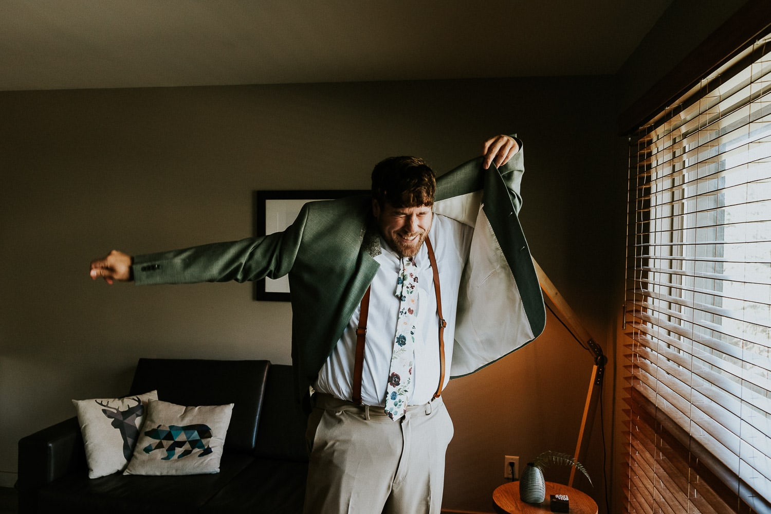groom with a silly expression trying to put on his suit jacket on his wedding day