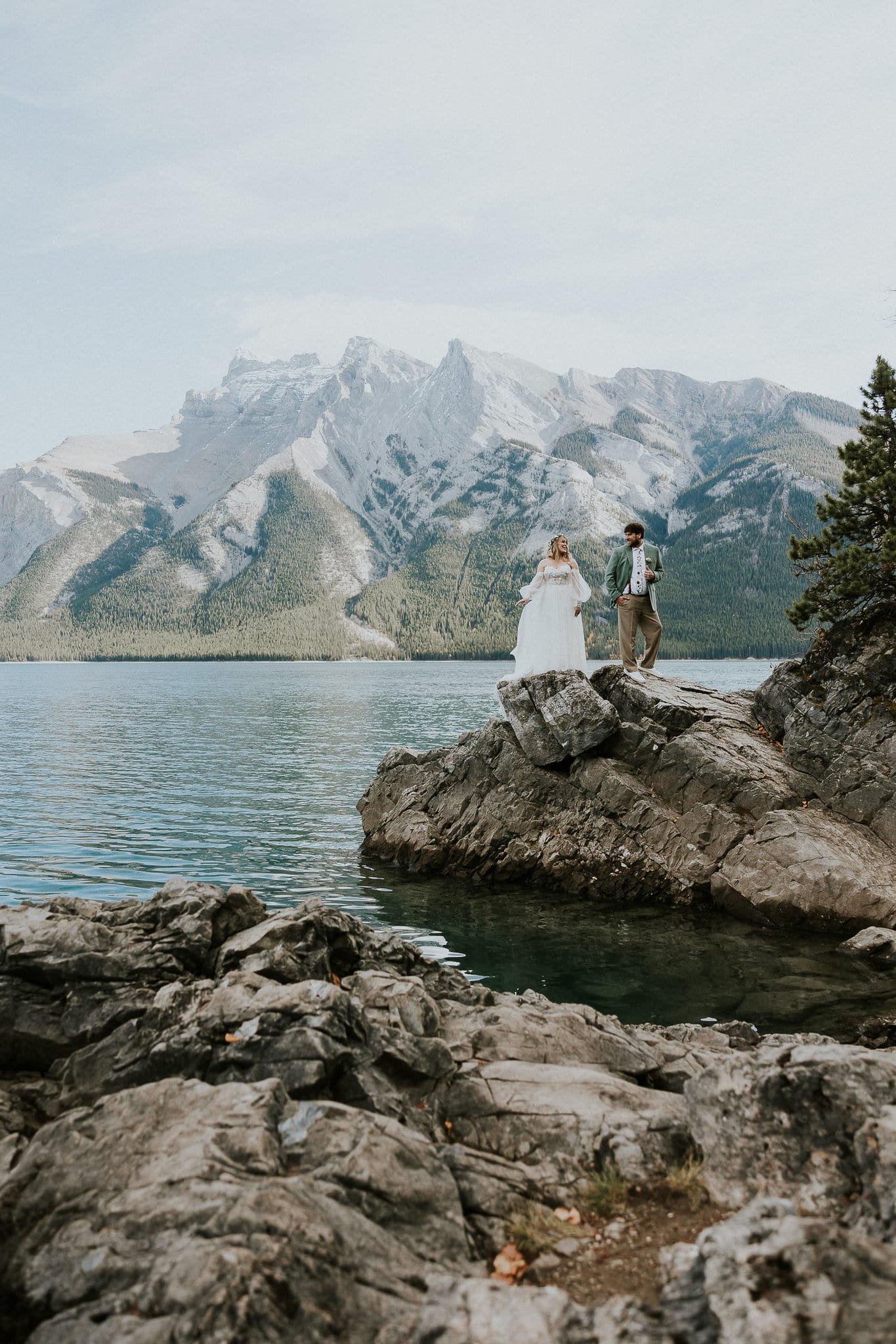 Courtney and mike stand on rocks at lake minnewanka in Banff national park on their wedding day.
