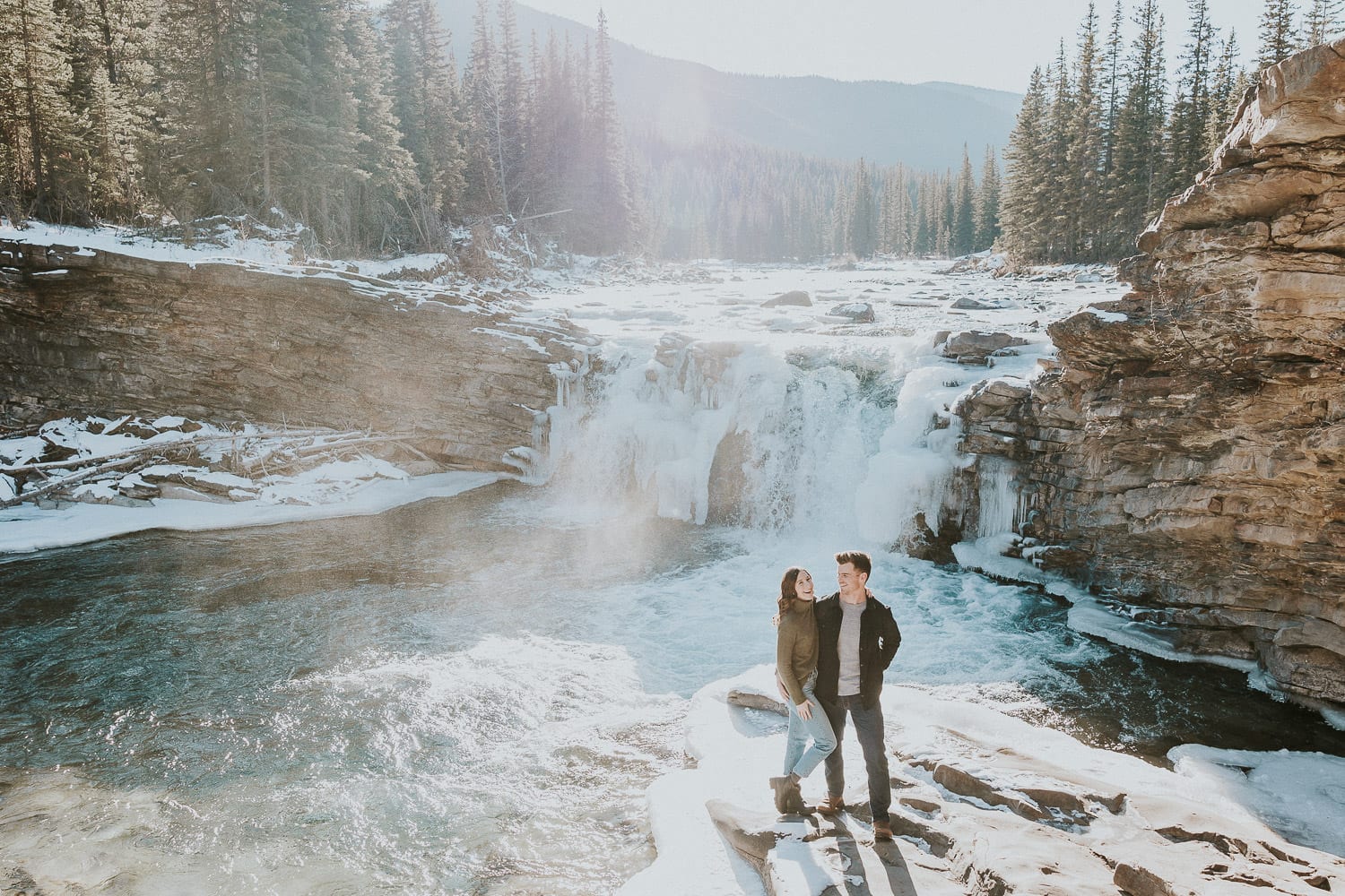 couple standing infront of frozen waterfall at sheep river falls in Kananaskis.