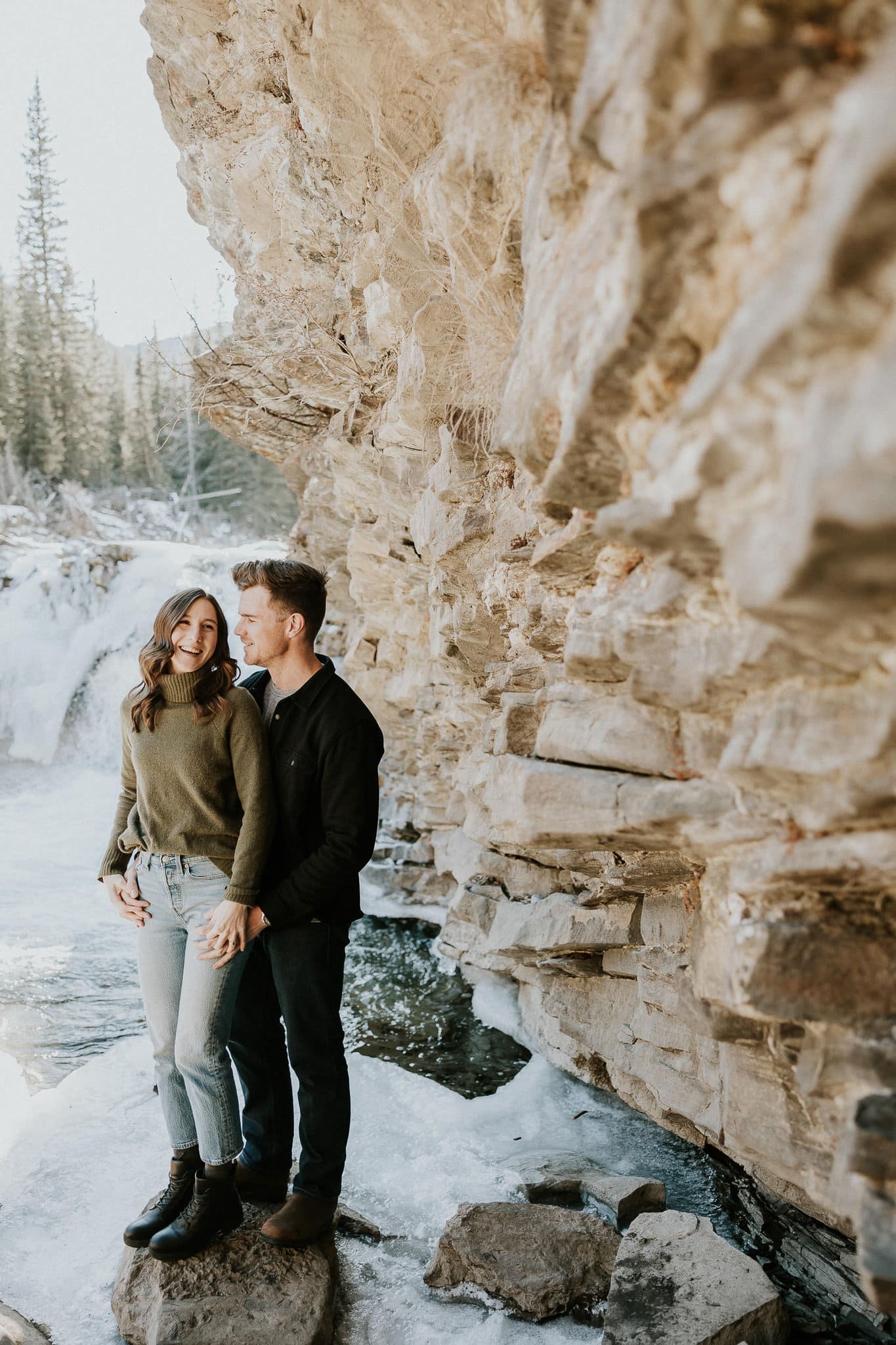 couple standing beside a mountain during their engagement photo shoot at sheep river falls.