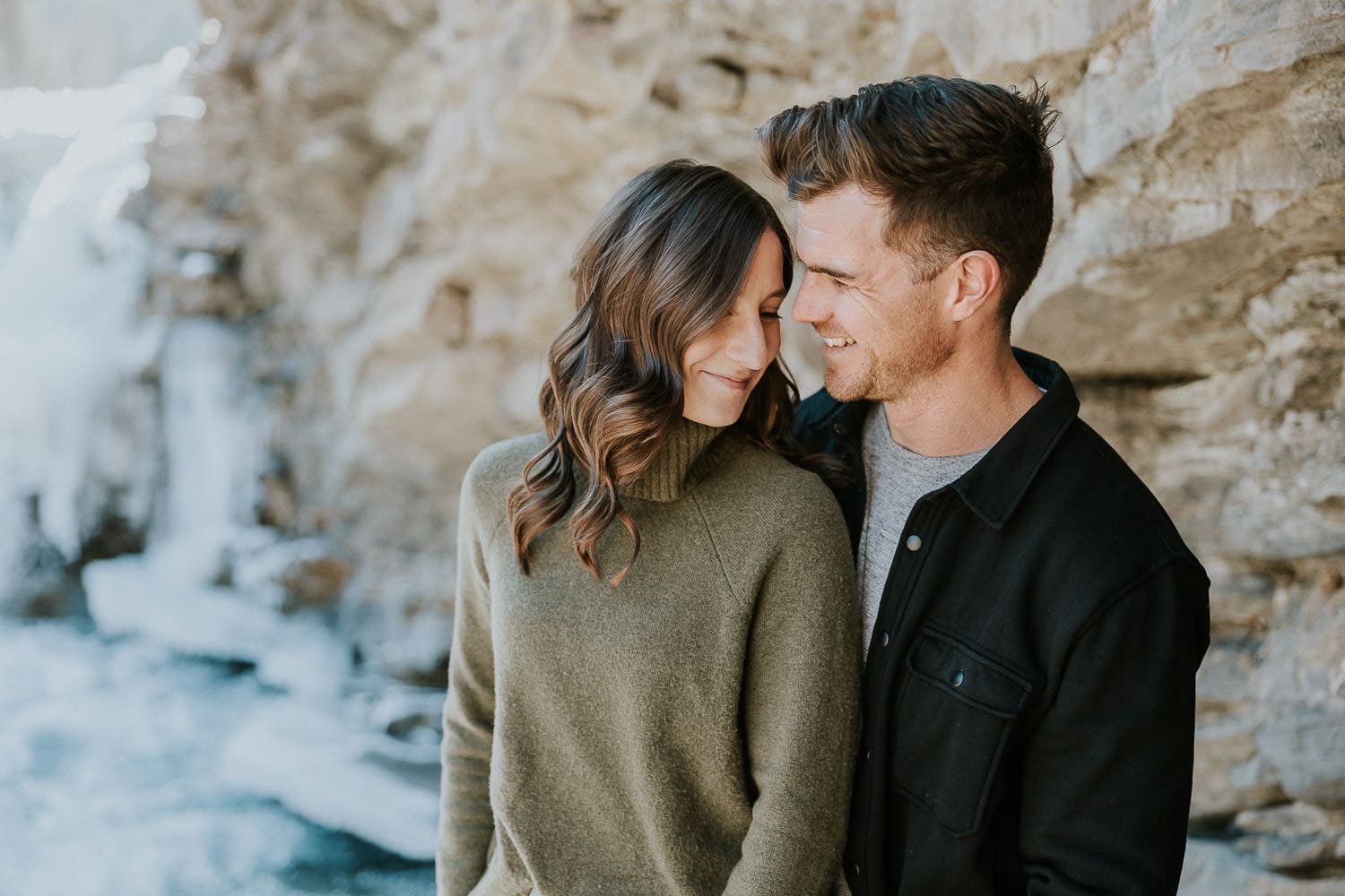 couple cuddling at sheep river falls during their engagement photo shoot.