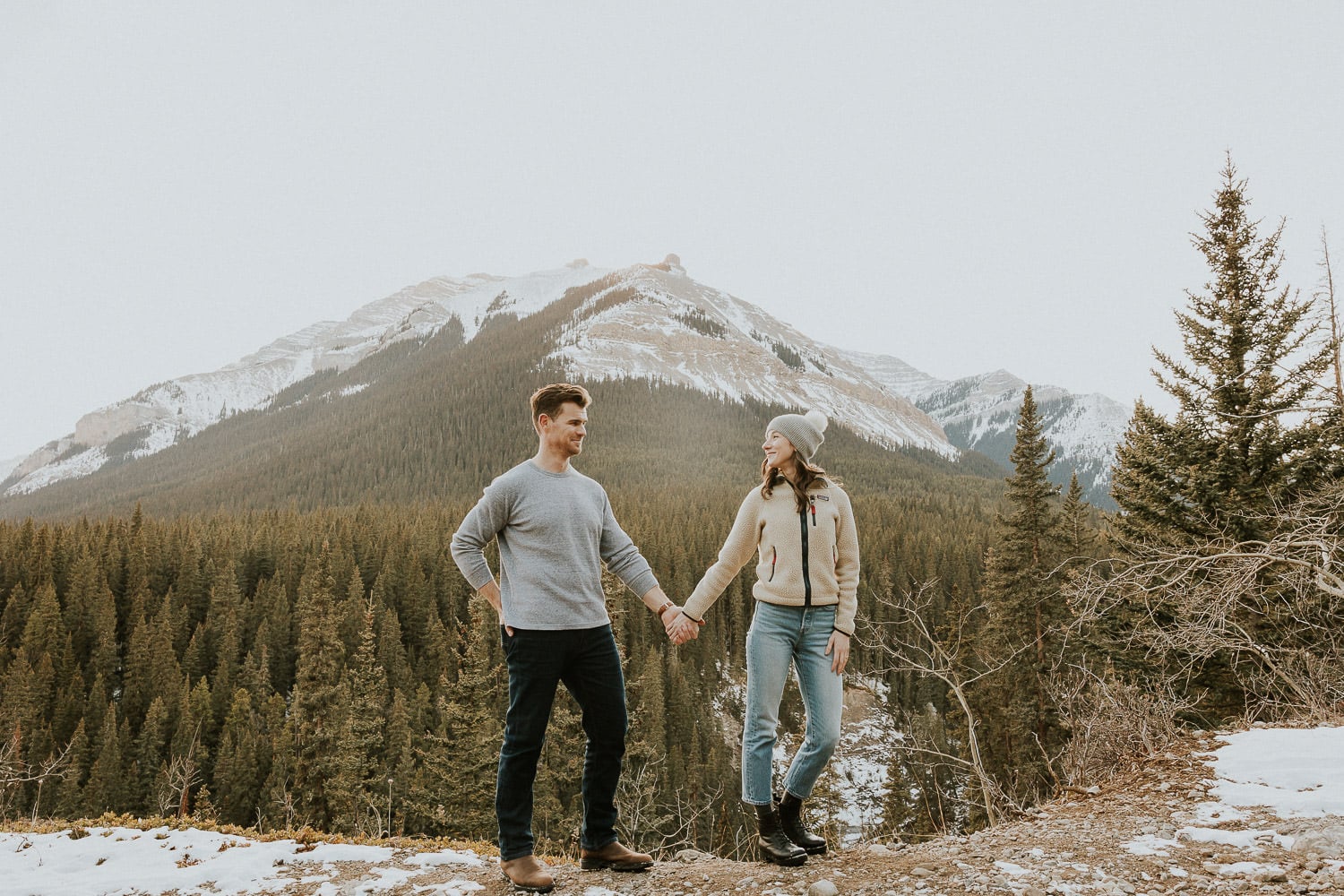 Couple stands hand in hand at Sheep River Falls for their engagement photo shoot in turner valley. 